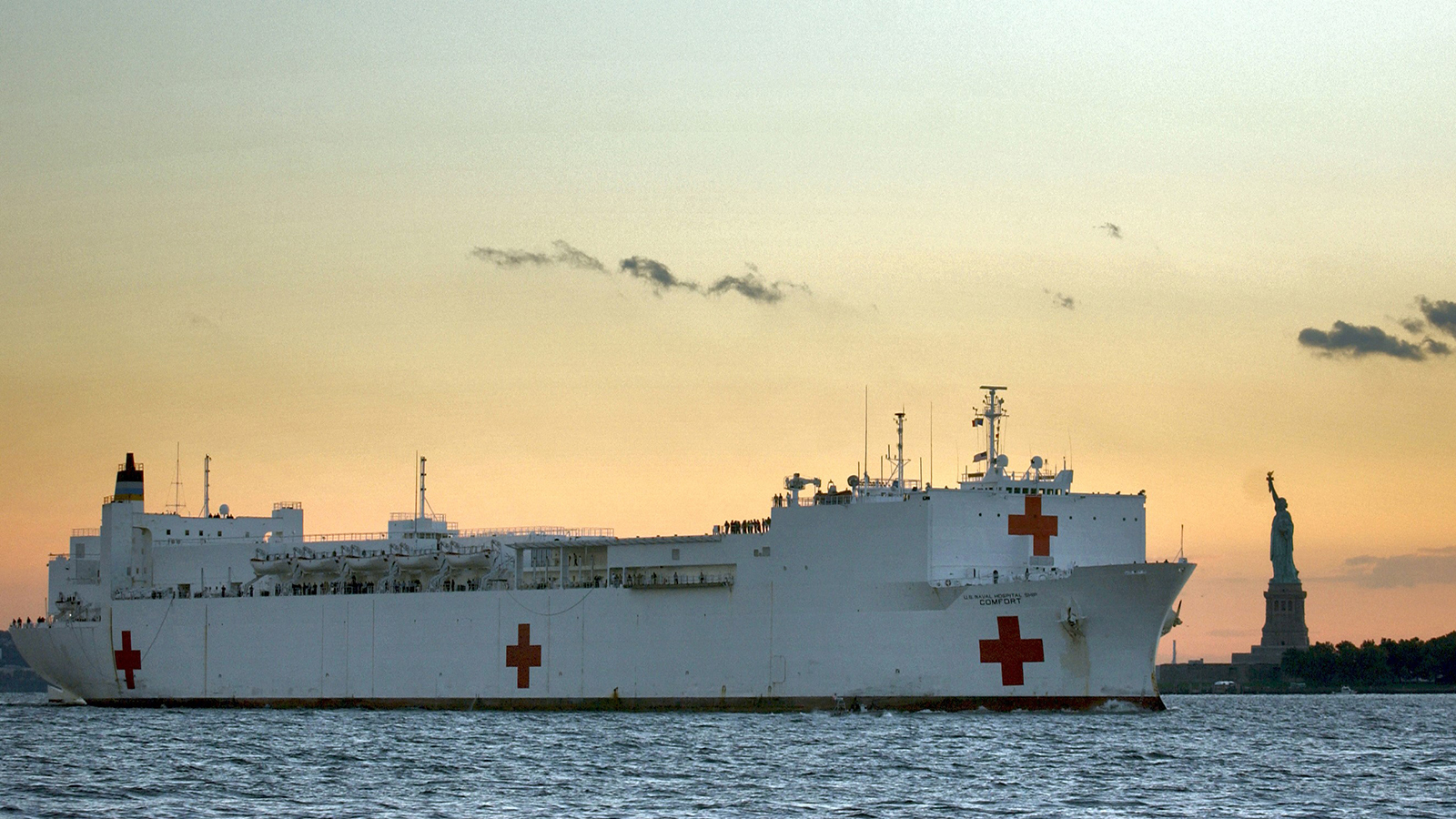 The USNS Comfort sails into New York Harbor with the Statue of Liberty in the background.
