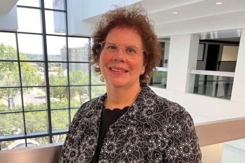 Karen Foli smiling in a patterned jacket beside a large window.