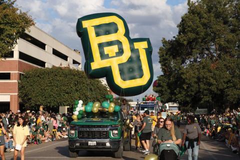 A green truck with a large BU logo carries students in a recent Homecoming parade.