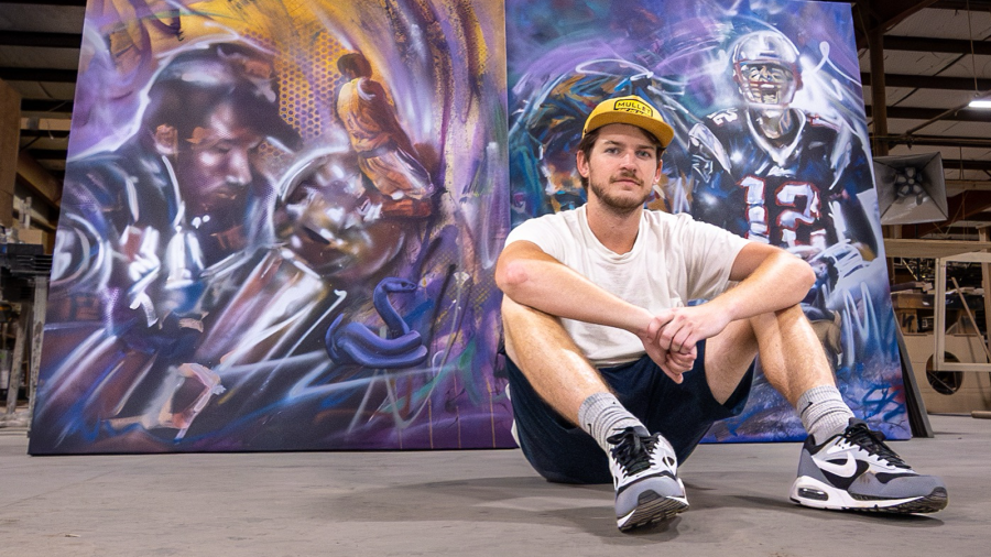 Artist Cade Kegerreis, seated in front of commission portraits of Kobe Bryant and Tom Brady