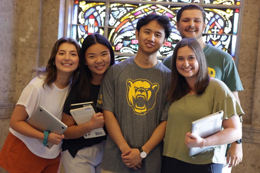Students stand in front of chapel stained glass before heading to class.