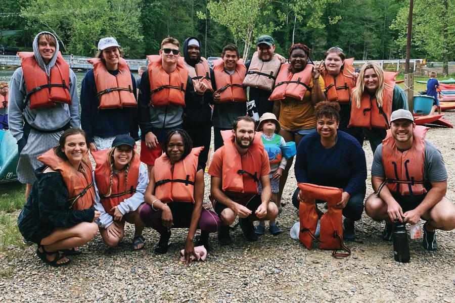 Baptist Student Ministries members in orange life jackets pose together beside a river